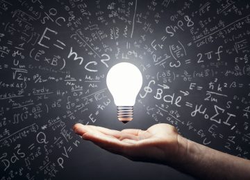 Still life photography of a hand and a floating, lit light bulb. Smudged blackboard background.